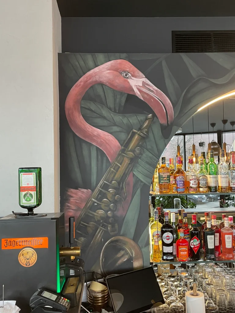Mural na zlecenie restauracji Melomania przy filharmonii Zielonogórskiej przestawiajacy flamingi z instrumentami muzycznymi